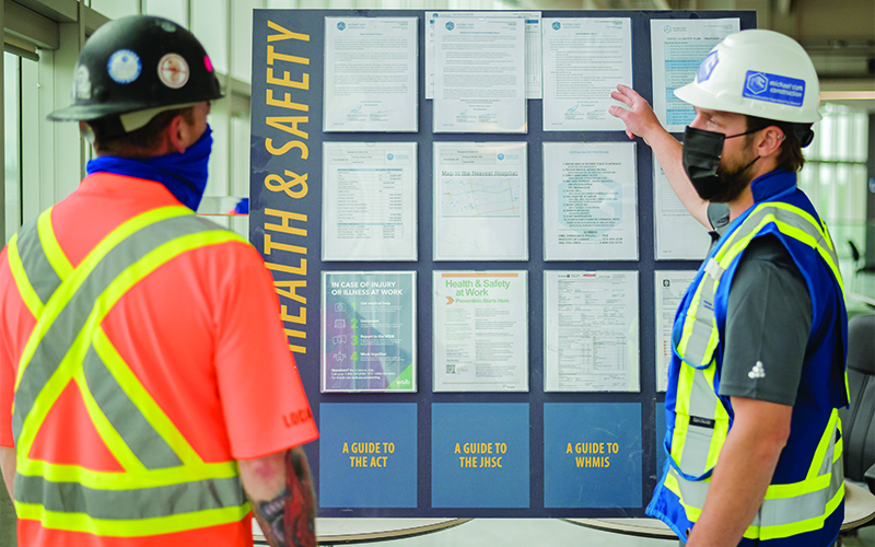 two construction workers discussion a health and safety board at a project site.